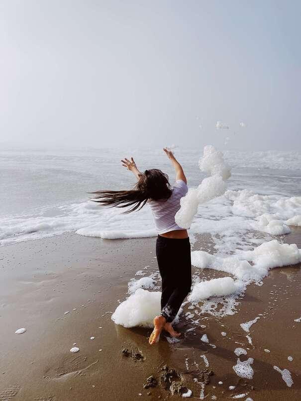 Une femme danse pieds nus dans l’écume, sur une plage