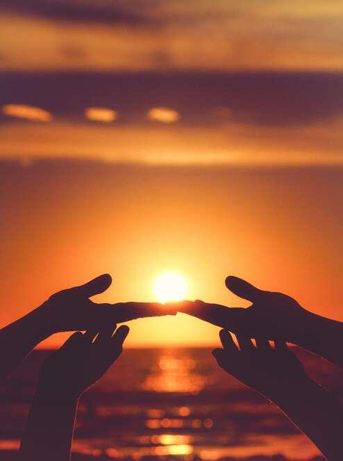 Deux mains se rejoignent devant un soleil couchant sur la mer